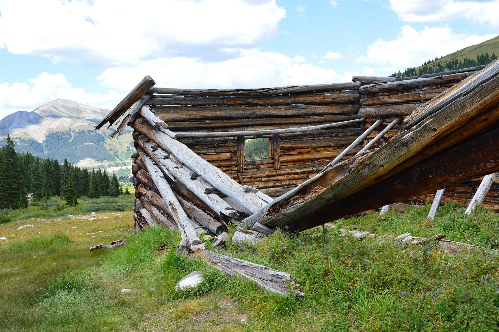 Collapsed wooden cabin in a grassy mountain meadow under a cloudy sky, The ruins of an old cabin, Mayflower Gulch, Colorado