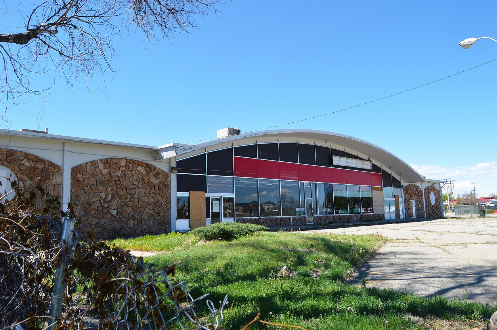 Modern building with a curved roof, red awning, and glass entrance beside a grassy area and parking lot