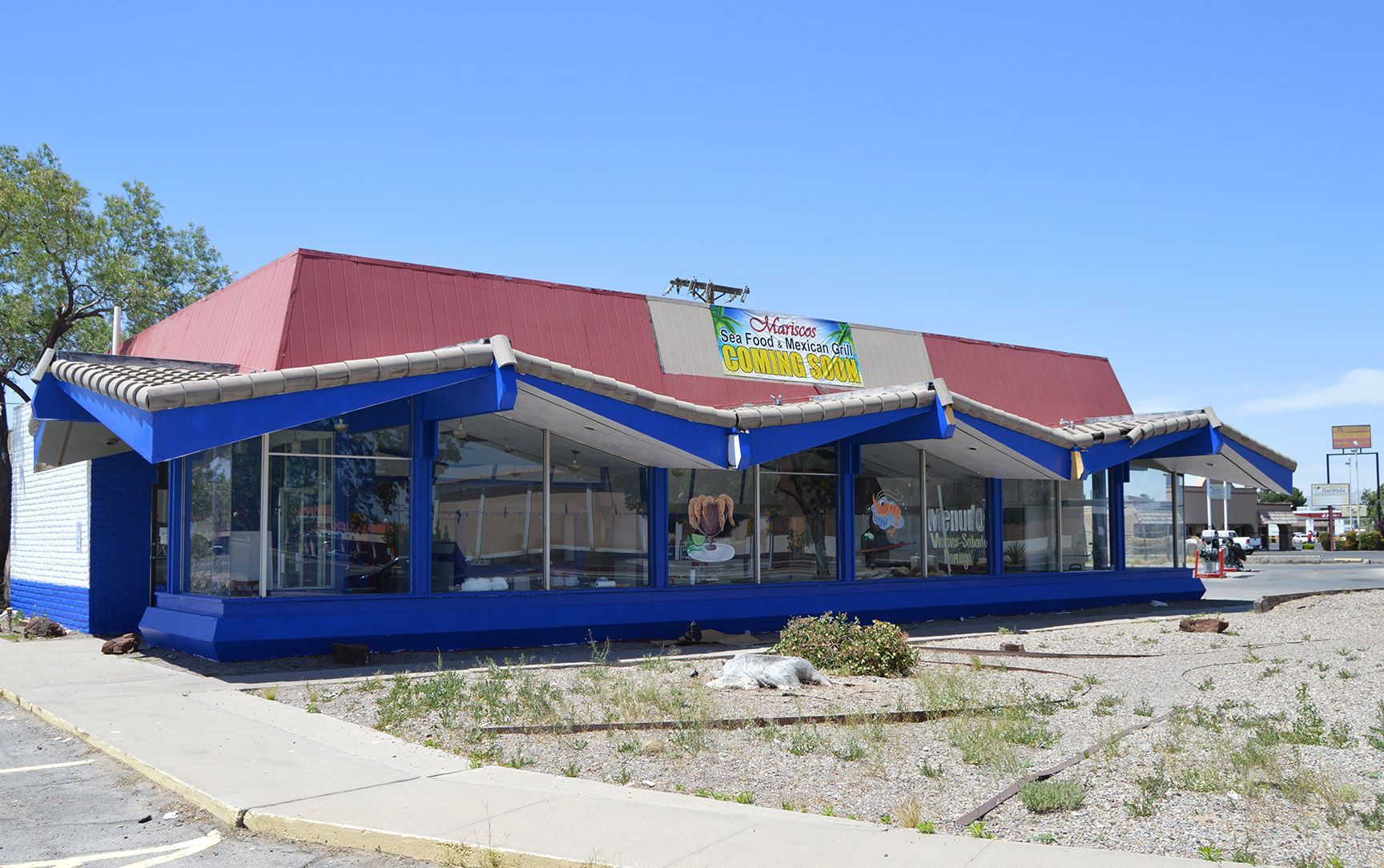 Blue-roofed roadside restaurant with large windows and gravel parking lot under a clear sky