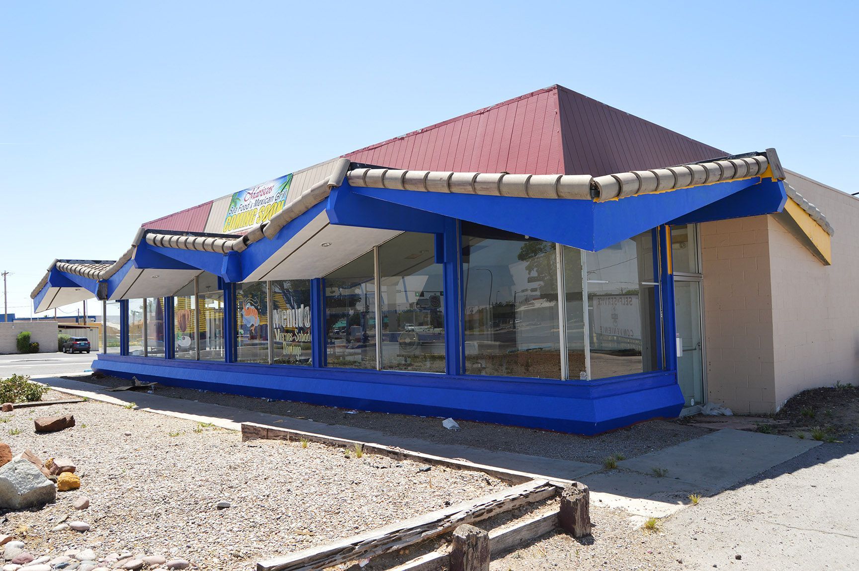 Blue storefront with glass windows and awnings on a sunny gravel lot
