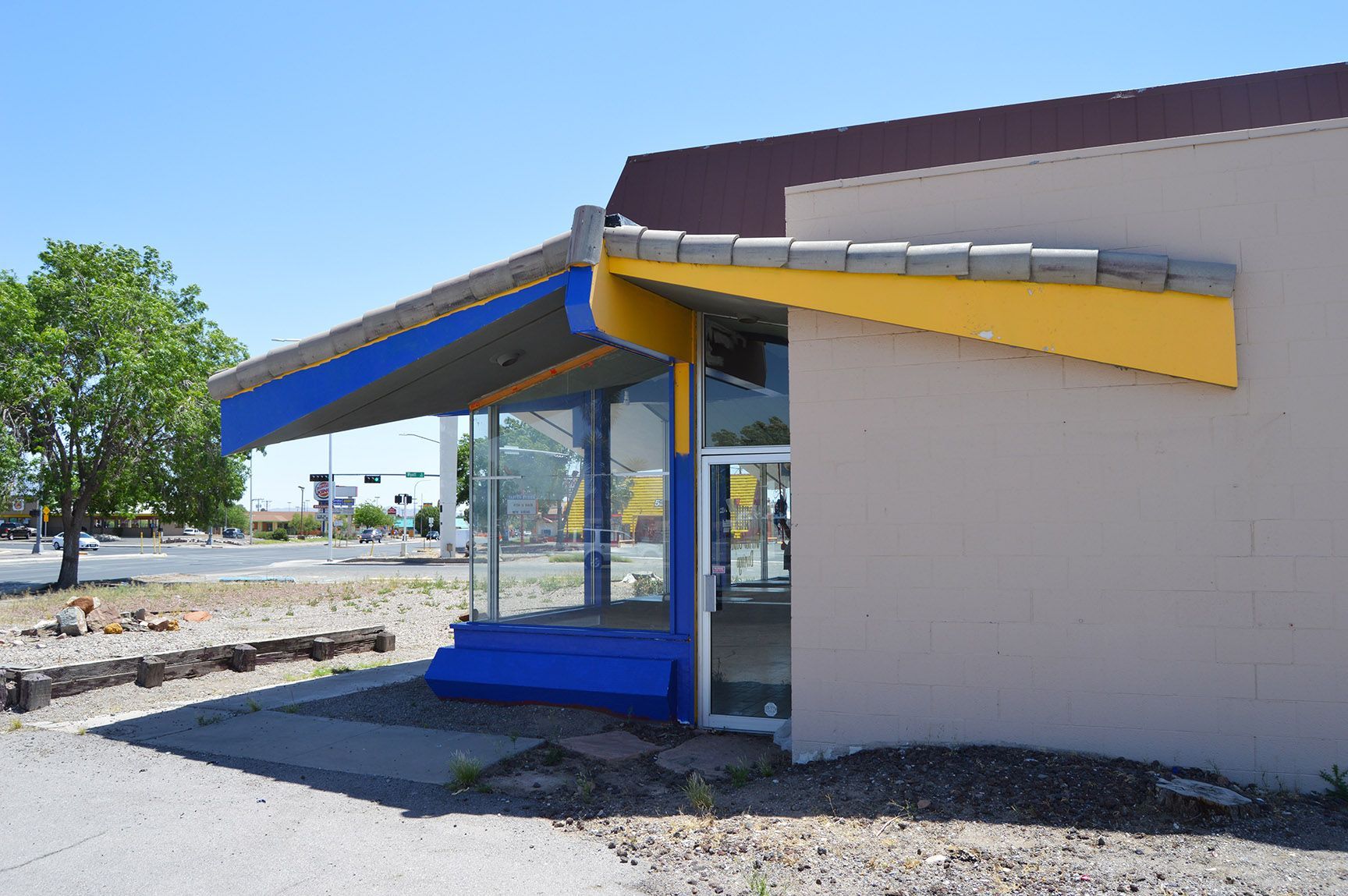 Small roadside building with blue and yellow awning beside a gravel lot under a clear sky