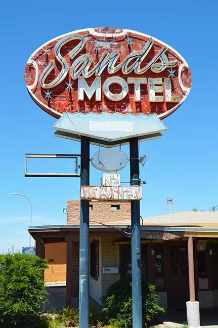 Sands Motel sign on a pole against a blue sky, above a low roadside building
