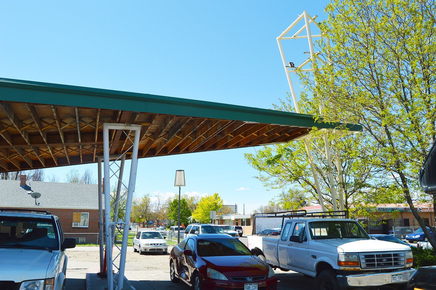 Covered parking lot with several parked cars under a green-roof canopy on a sunny day
