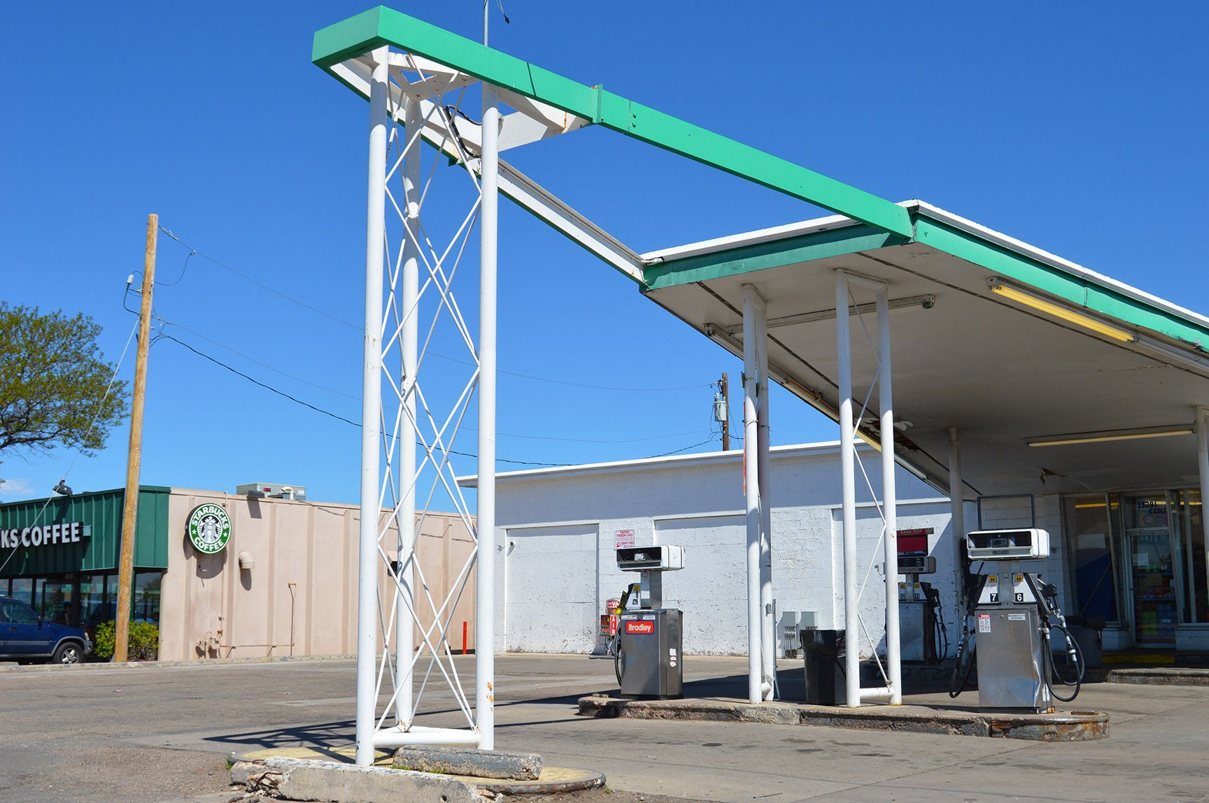 Abandoned gas station canopy and pumps under a blue sky, with utility poles and buildings nearby