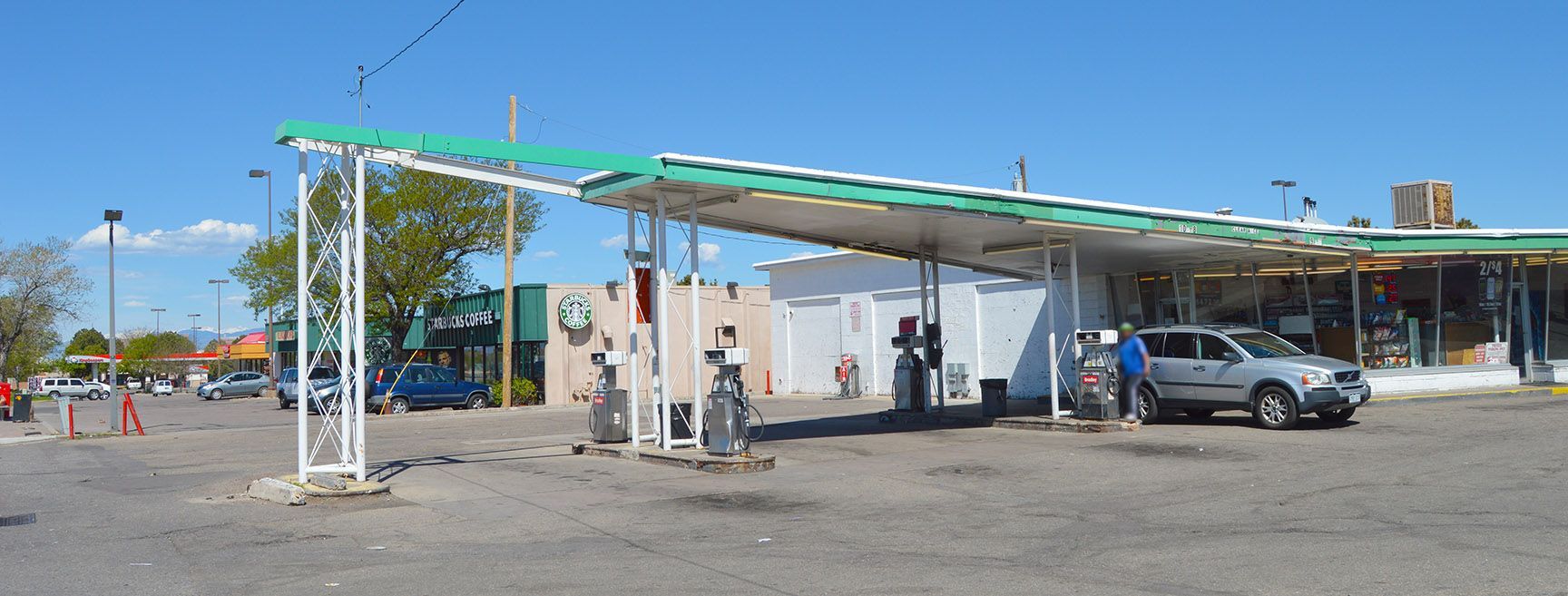 Gas station canopy with a car, a few people, and a clear blue sky.