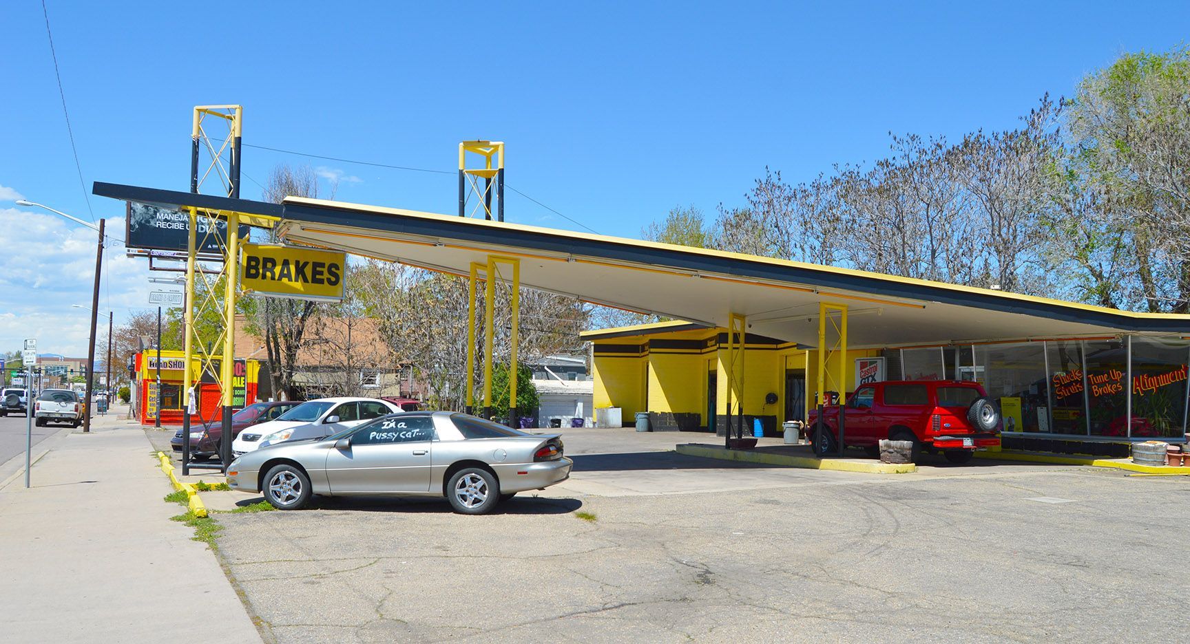 Outdoor car wash with several cars under yellow wash bays on a sunny day