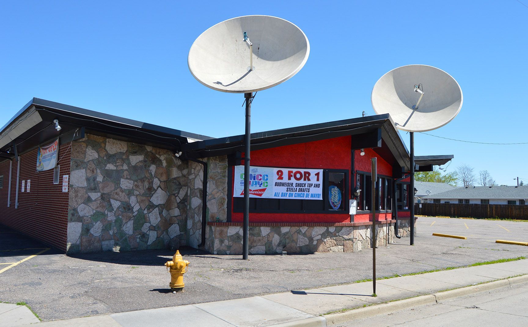 Corner storefront with red awning and stone wall, two large satellite dishes, and a yellow fire hydrant on the sidewalk