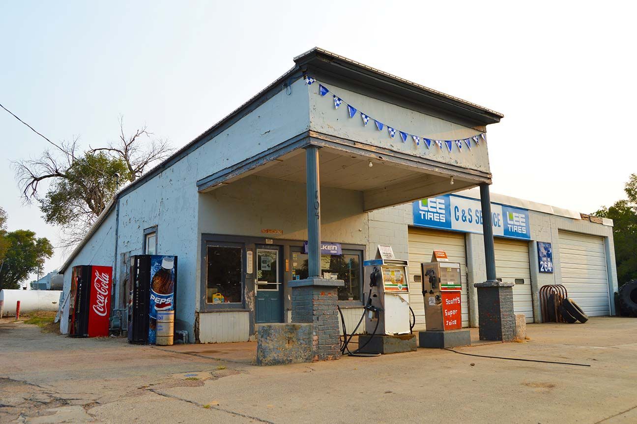 Small roadside convenience store with blue awning, vending machines, and a parked motorcycle at dusk