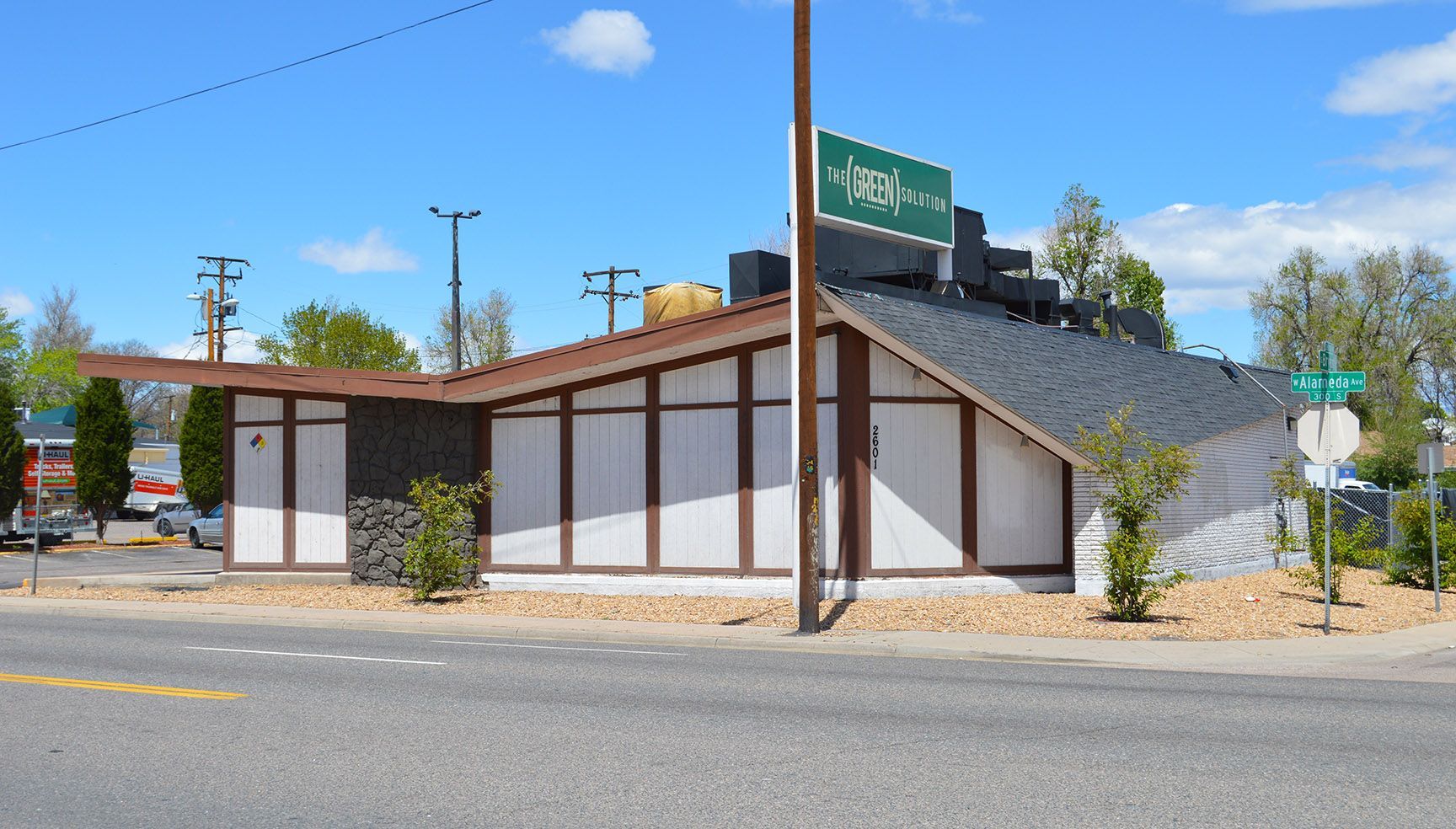 Low, tan-and-brown roadside building with a green sign under a clear blue sky