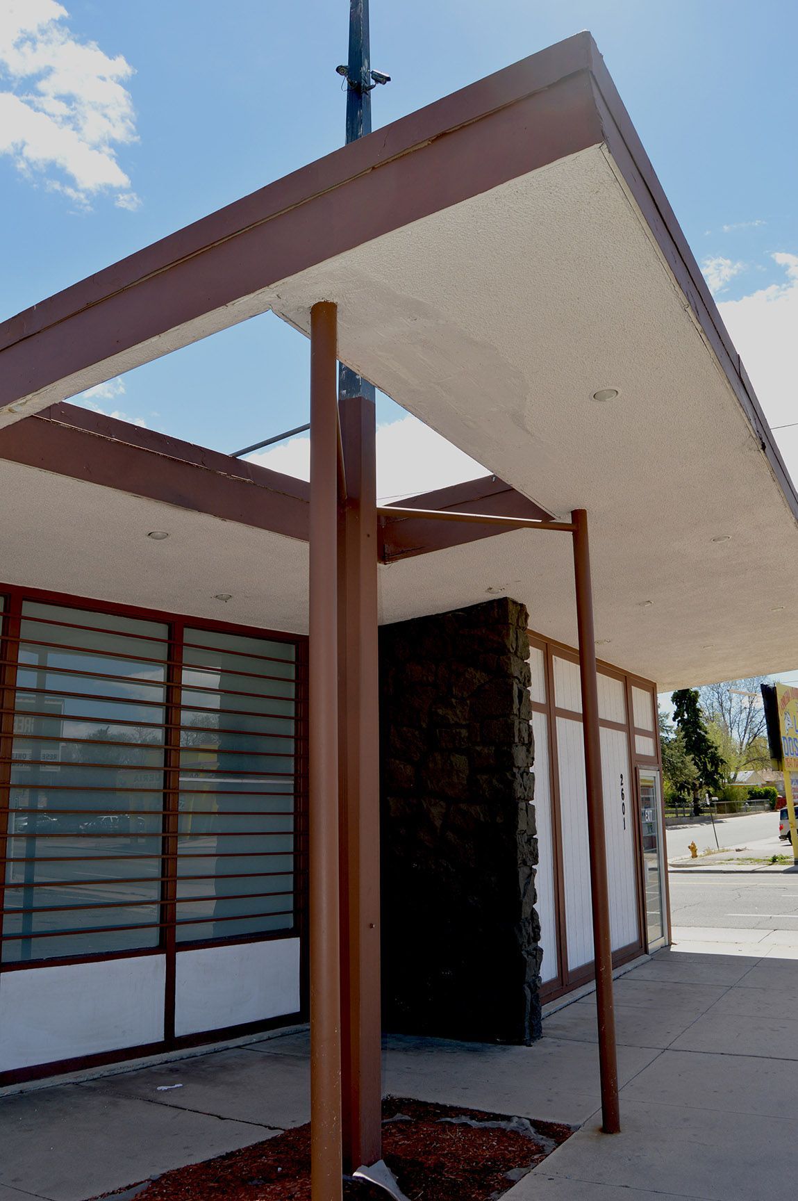 Modern building entrance with angled awning, red columns, and large windows under a blue sky