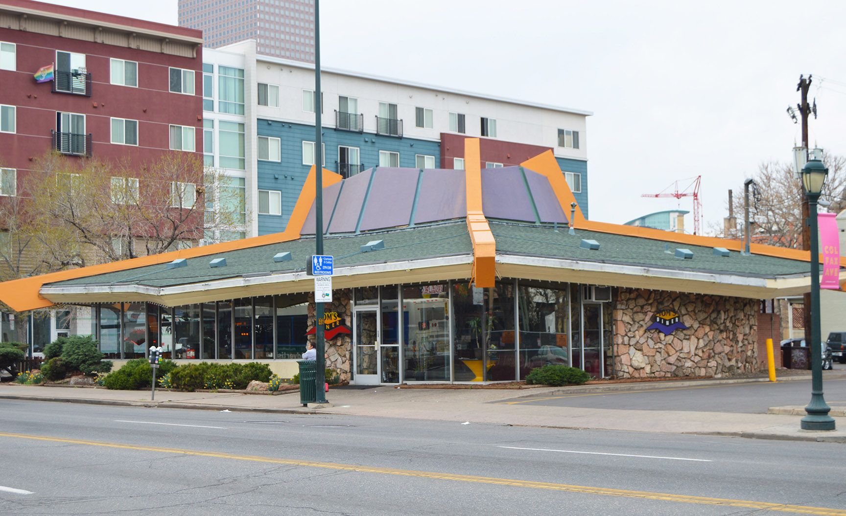 Corner café with orange-and-blue awnings on a city street beside apartment buildings and a crosswalk sign