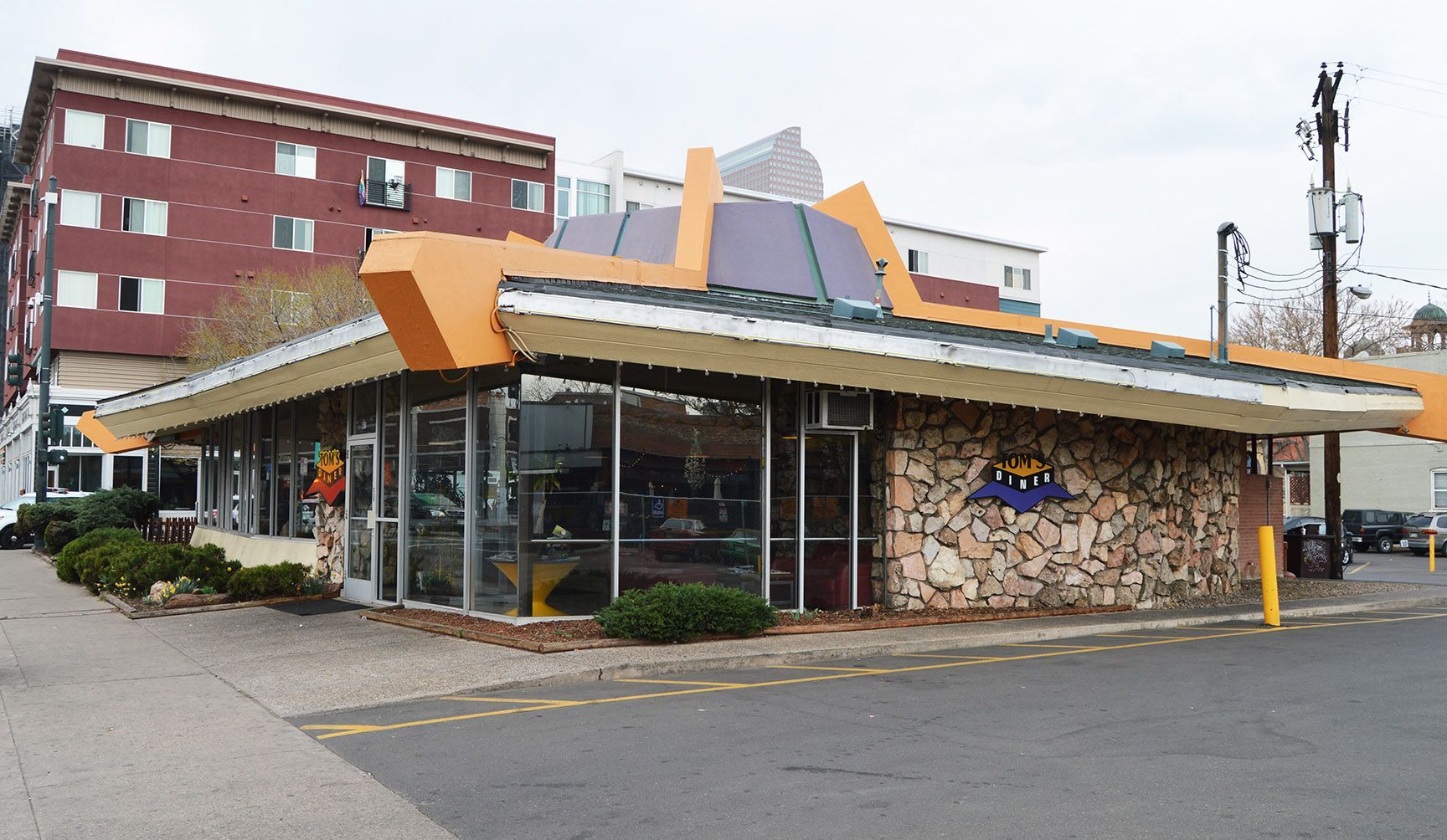 Street-side storefront with stone facade, large windows, and yellow awning on a cloudy day
