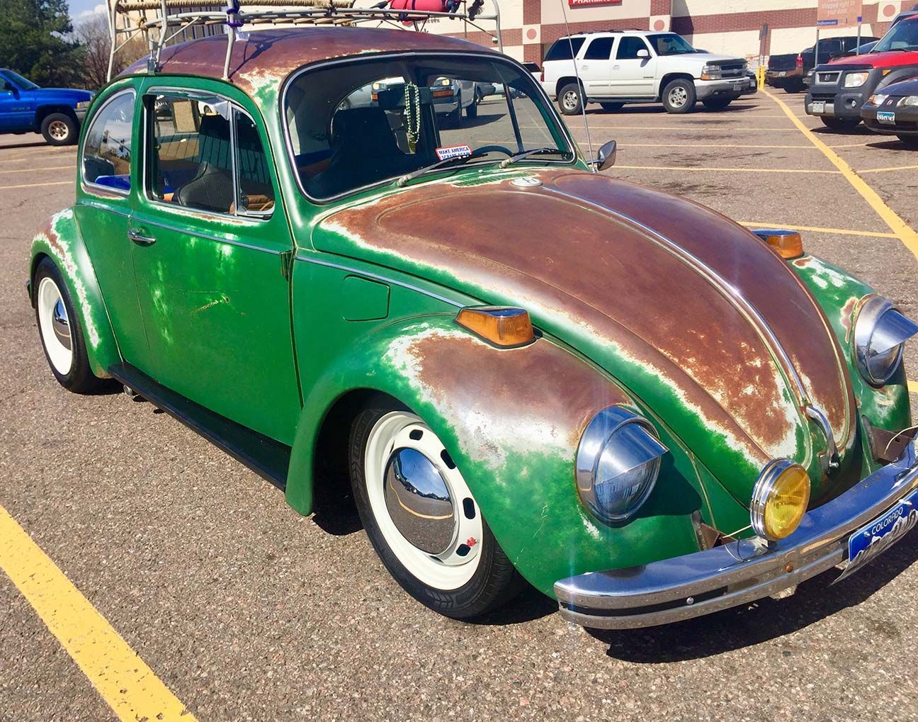 Green vintage Volkswagen Beetle with a rusted hood, parked in a lot on a sunny day, Englewood, Colorado