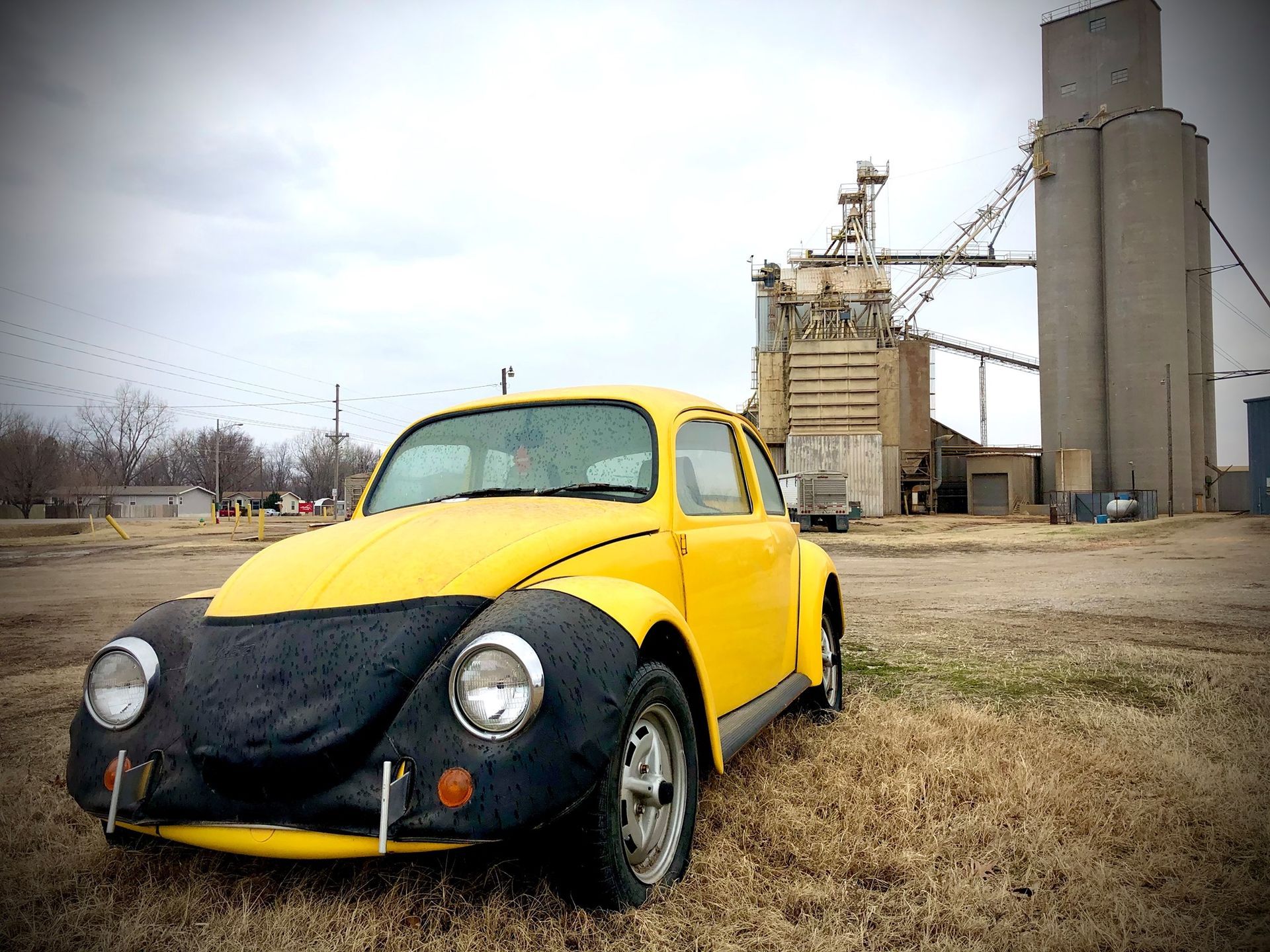 Yellow vintage car with black hood parked on gravel near an industrial plant, VW bug, Volkswagen, McPherson, Kansas