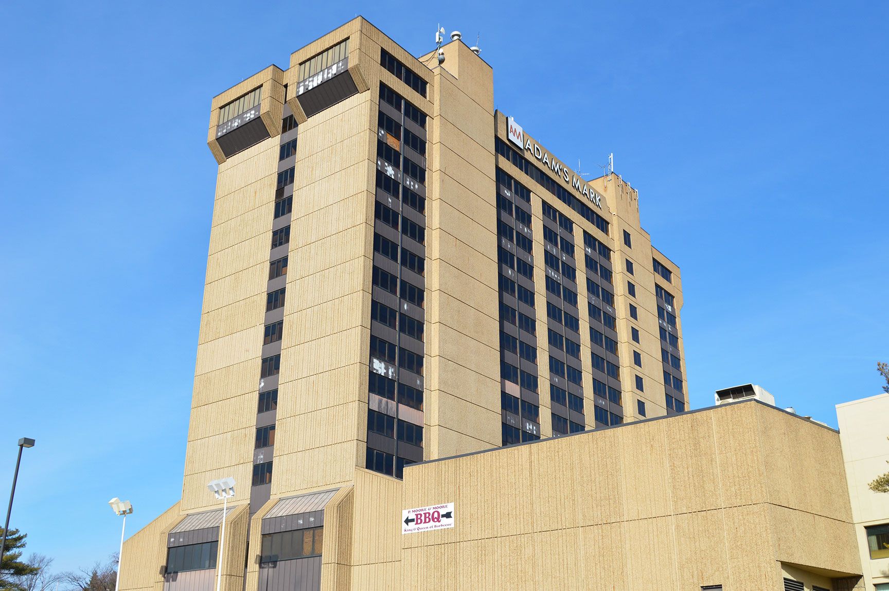 Tall beige office building against a clear blue sky, with a lower beige structure in front