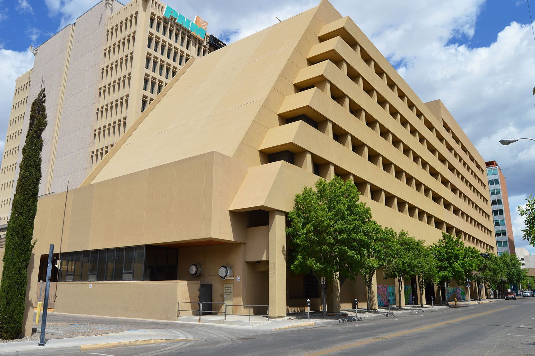 Modern beige office building on a city street with trees and a blue sky