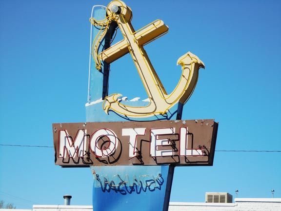 Gold anchor motel sign with blue sky background and graffiti on the lower panel