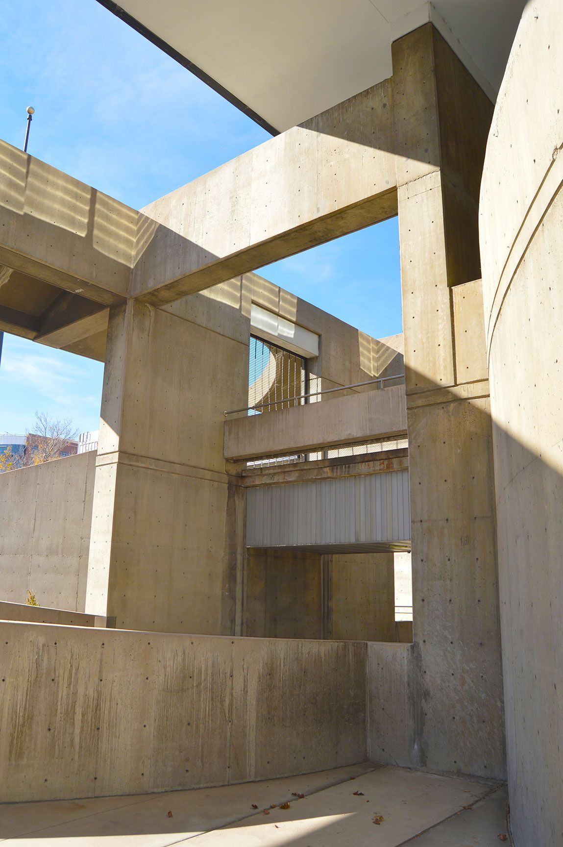 Concrete architectural structure with geometric beams and open sky overhead, lit by sunlight.