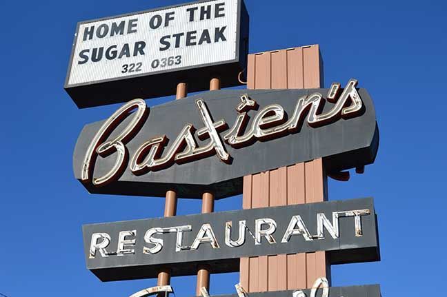 Bastien's restaurant sign with “Home of the Sugar Steak” against a blue sky