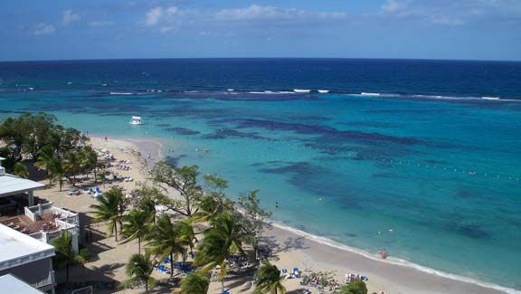 Tropical beach with turquoise water, white sand, palm trees, and a few people along the shore