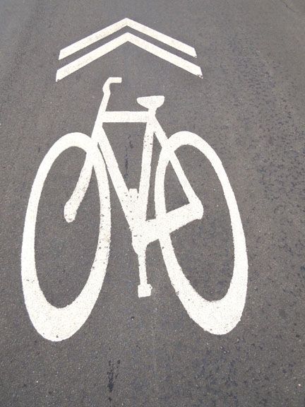 White bicycle symbol with upward chevrons painted on gray pavement