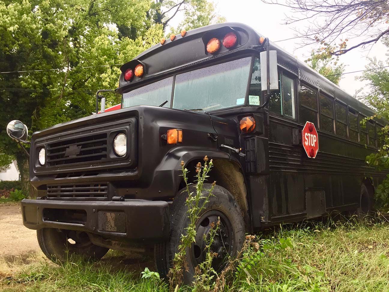 Black school bus parked in grass, viewed from the front-left under trees, McPherson, Kansas