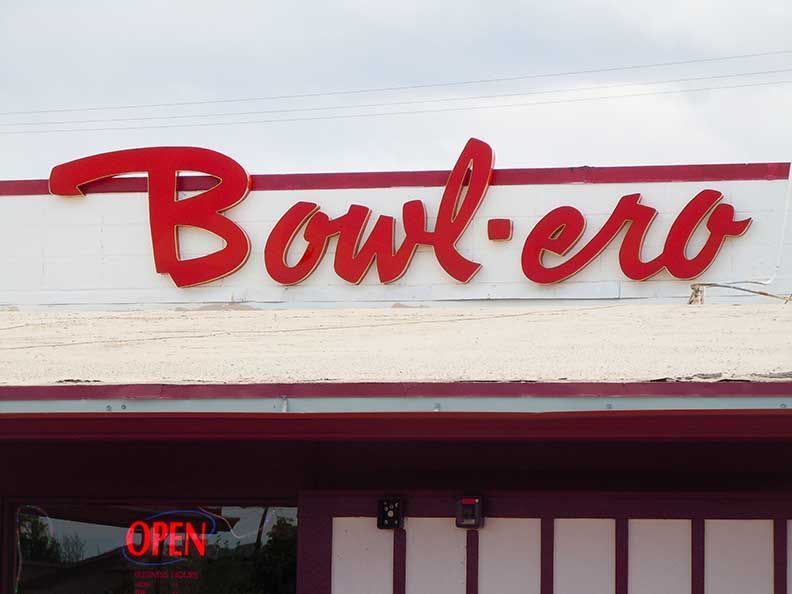 Red Bowlero bowling alley sign above an entrance with a small neon “OPEN” sign below