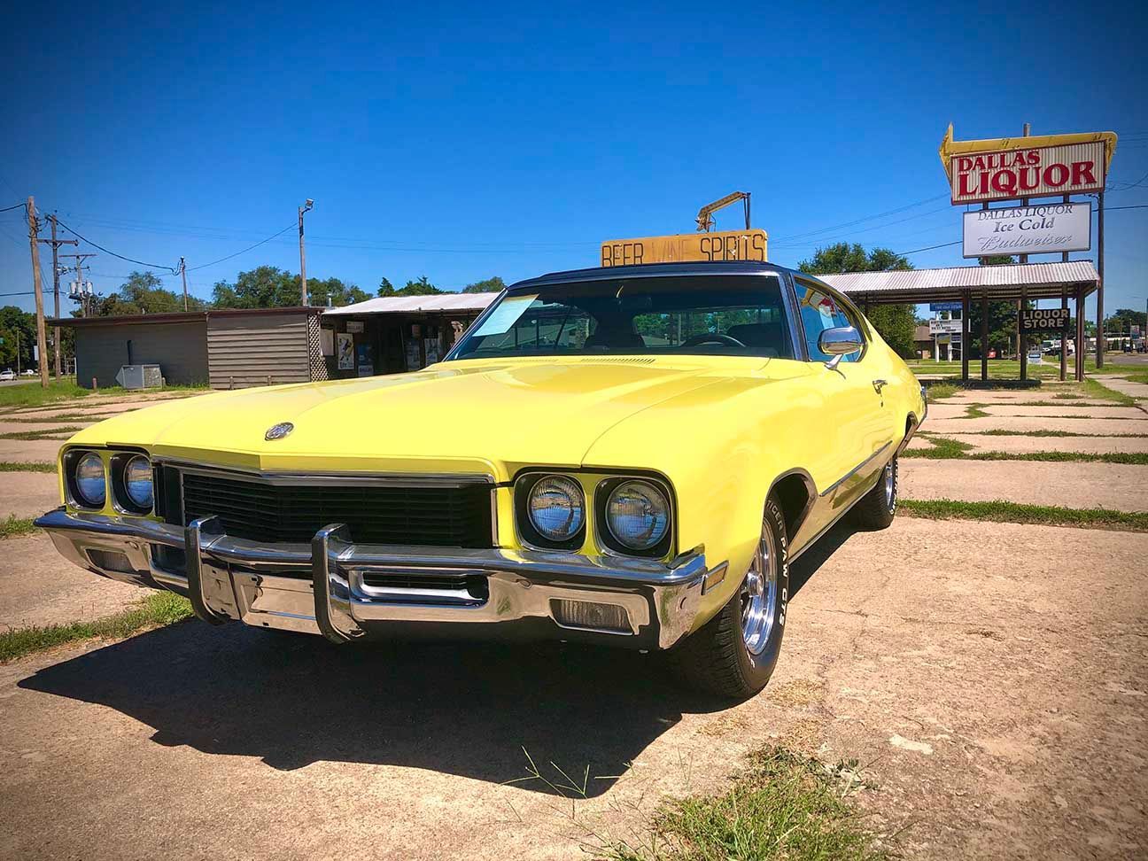 Yellow classic car parked on a sunny roadside with a liquor store sign in the background, Buick Skylark, Salina, Kansas