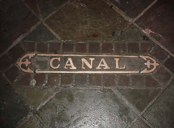 Rectangular floor plaque labeled “CANAL” with arrows on a dark stone tile floor