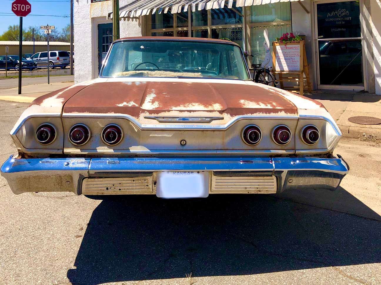 Rear view of a rusted vintage car parked on a sunny street outside a storefront, Chevy Impala, Chevrolet, Minneapolis, Kansas