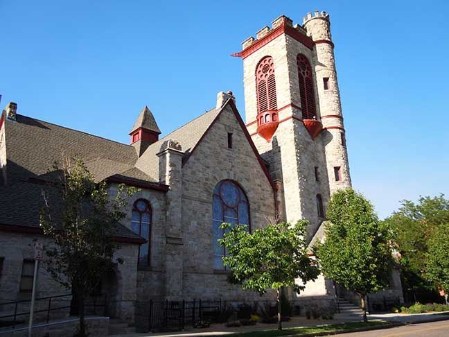 Stone church with red-trimmed tower and arched windows on a sunny day