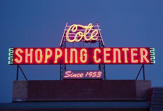 Neon sign for Cote Shopping Center with “Since 1953” on a building at dusk