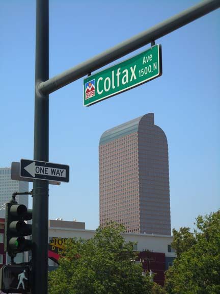 Colfax Ave street sign at a city intersection with a tall building in the background