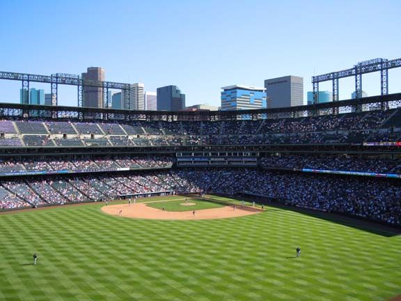 Baseball stadium with a green field, packed stands, and a city skyline in the background