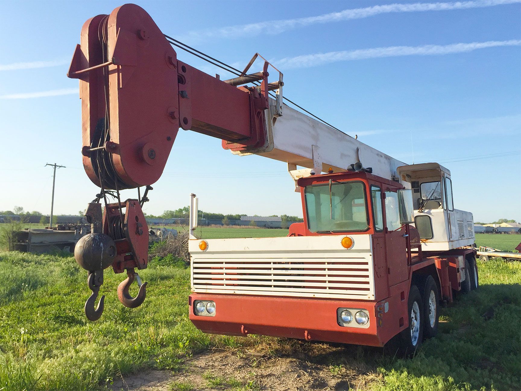 Red and white mobile crane parked in a grassy field under a blue sky