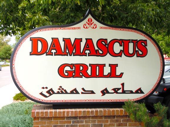 Damascus Grill restaurant sign with red lettering and Arabic text on a brick base outdoors