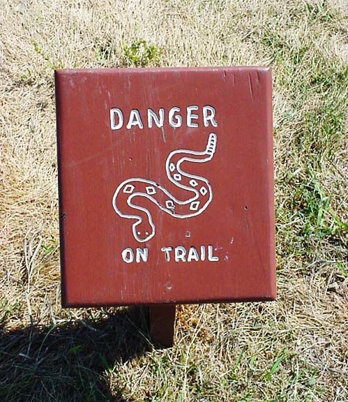 Red warning sign reading “DANGER ON TRAIL” with a snake icon in grassy area.