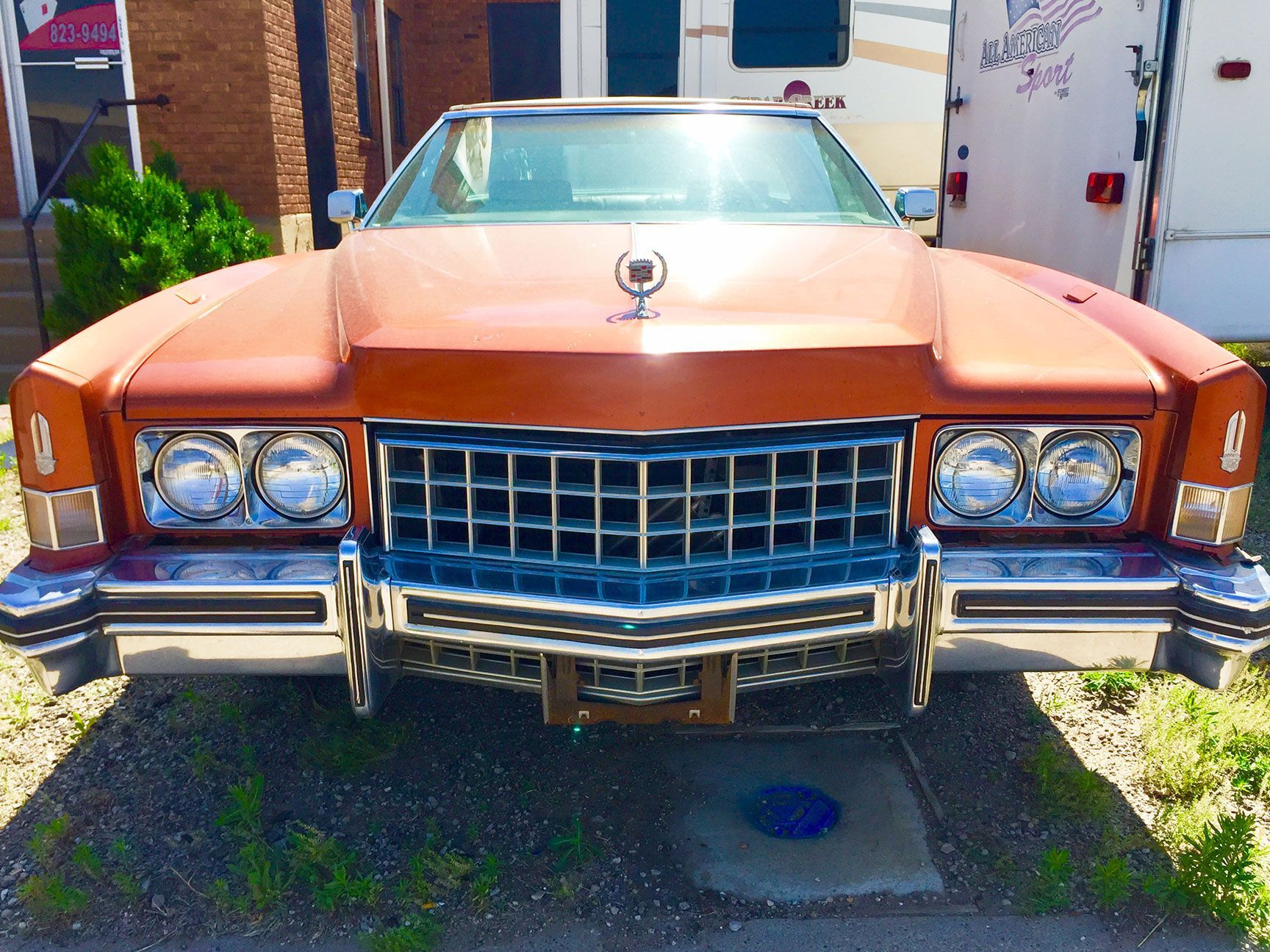 Front view of a vintage orange Cadillac parked in a driveway, with chrome grille and bumper.
