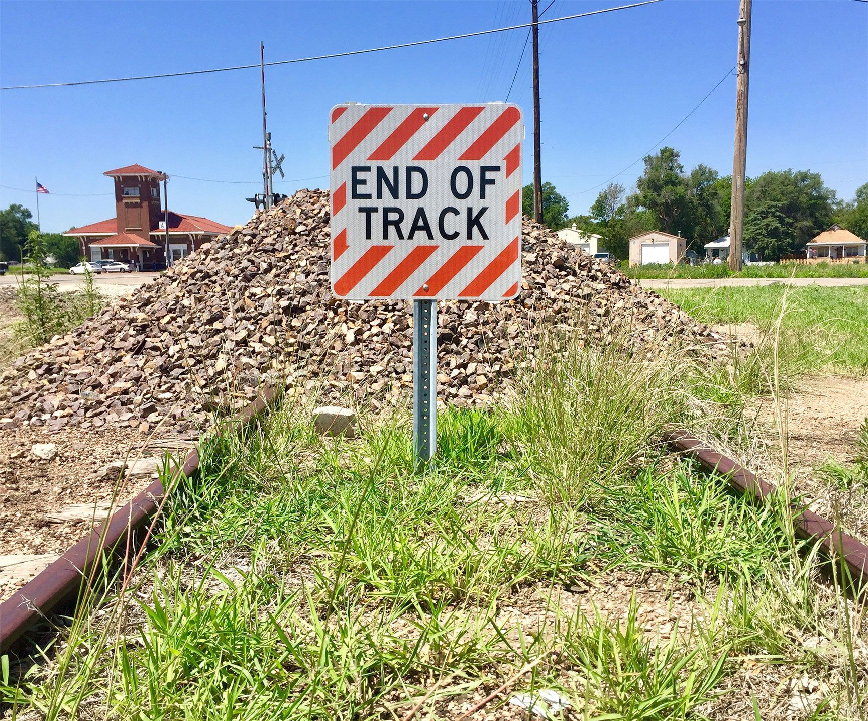 End of Track sign in front of a gravel pile beside railroad tracks under a blue sky