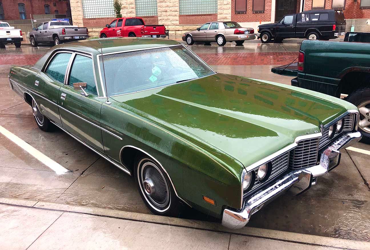 Green classic car parked on a wet street beside a brick building, front three-quarter view, Ford Galaxy, Salina, Kansas