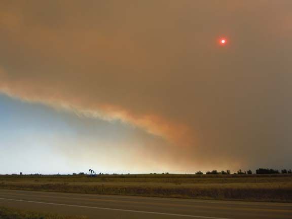 Dark storm cloud over flat fields with a red sun or light in the sky