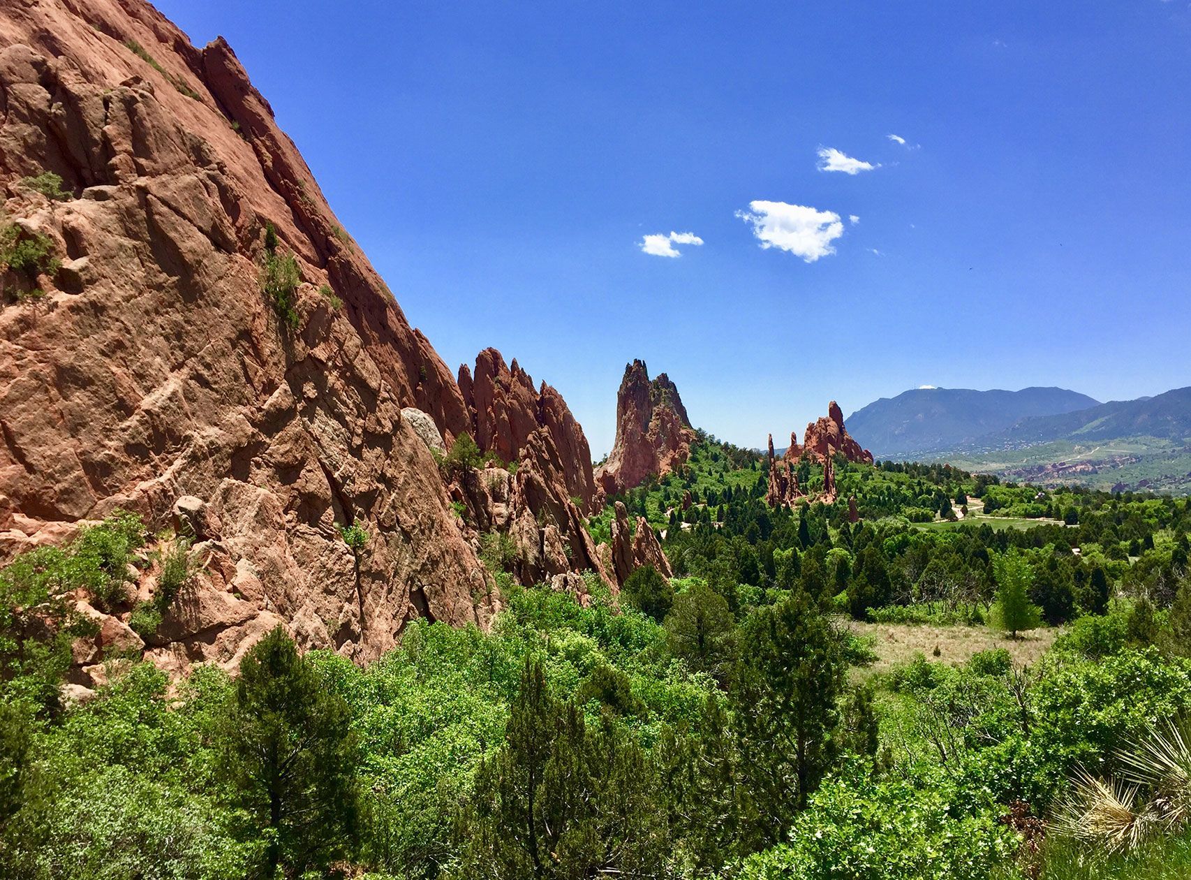 Rocky red cliffs beside a lush green valley under a bright blue sky, Garden of the Gods, Colorado Springs, Colorado