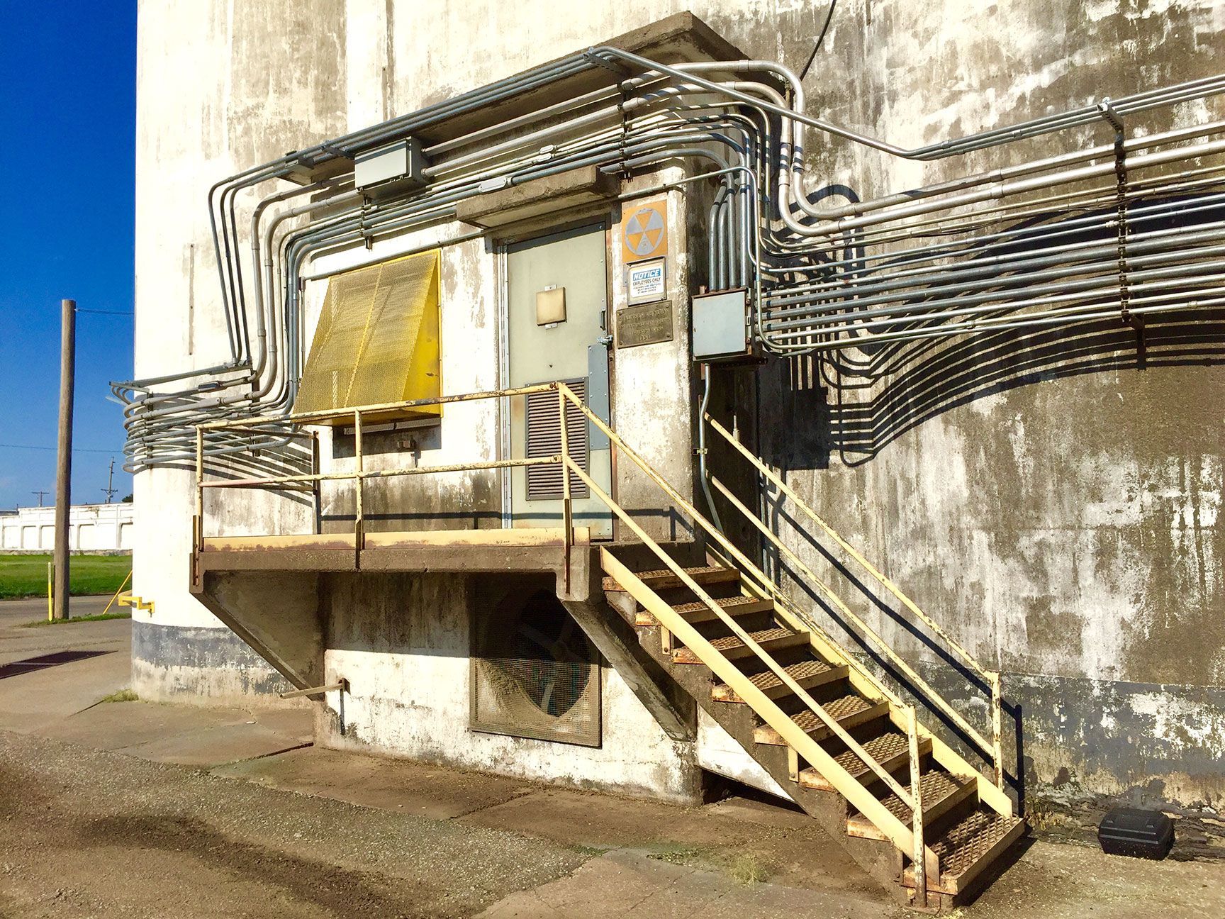 Industrial building with yellow stairs and pipes on a concrete exterior wall under a blue sky