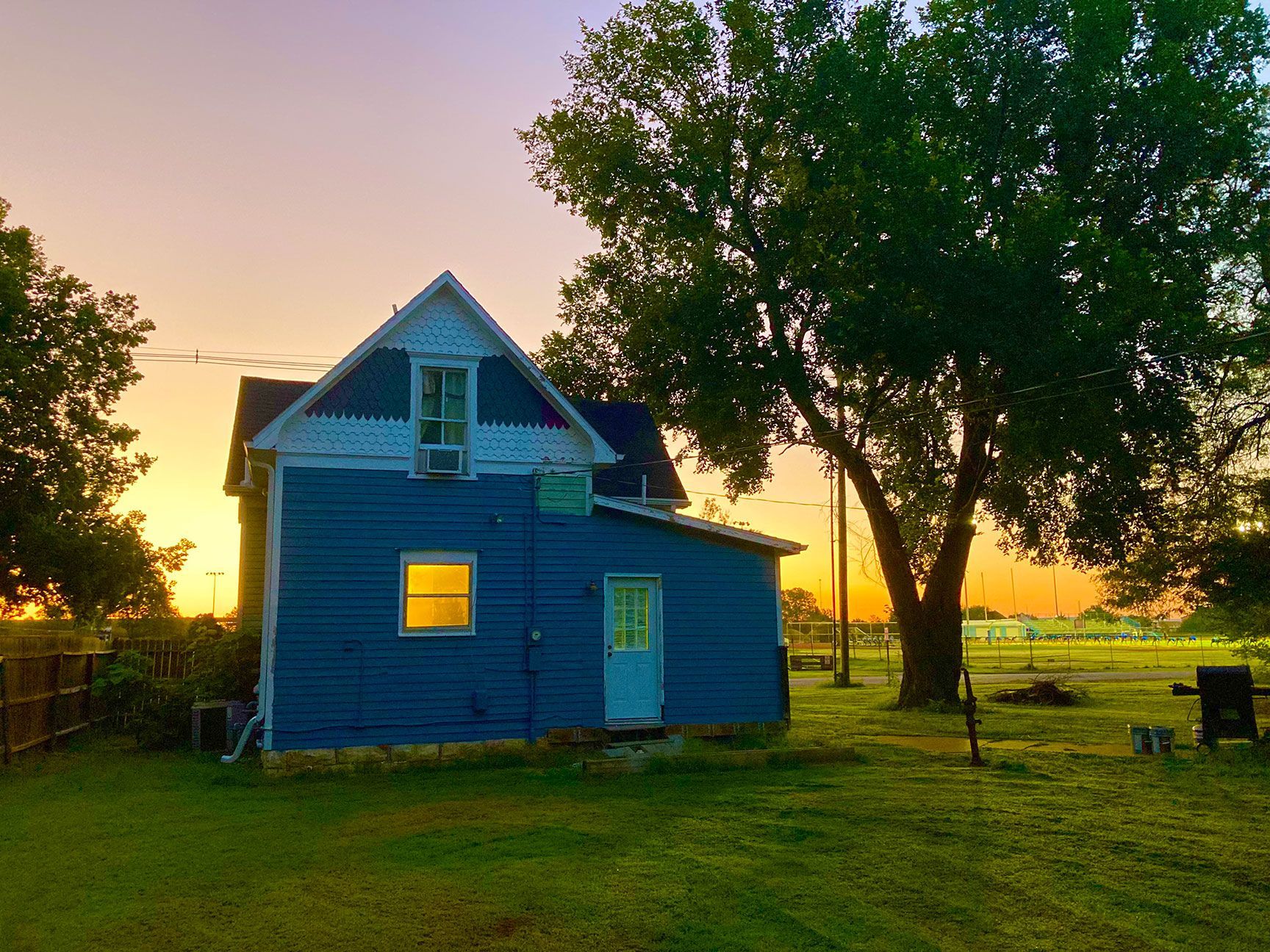 Blue house at sunset beside a large tree in a grassy yard