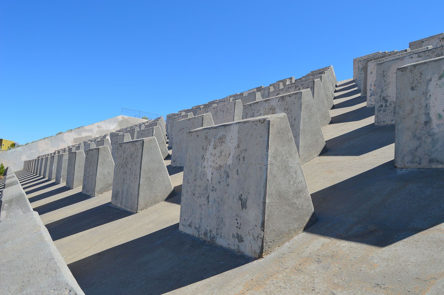 Concrete wave breakers lined up along a sunny shoreline under a clear blue sky