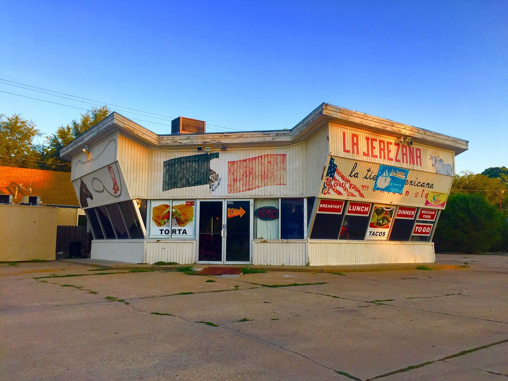 Small roadside building with faded murals and a large “La Jer...” sign at dusk