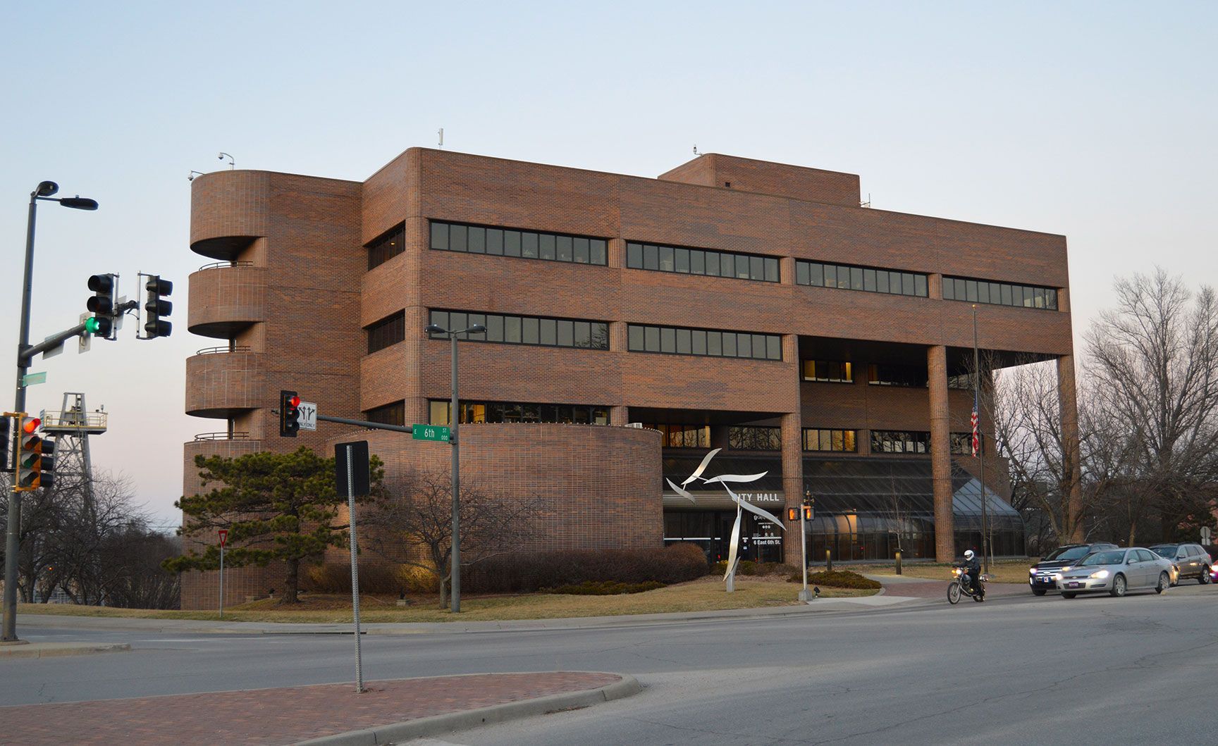Brick office building at a street corner with traffic lights and a few cars in the evening.