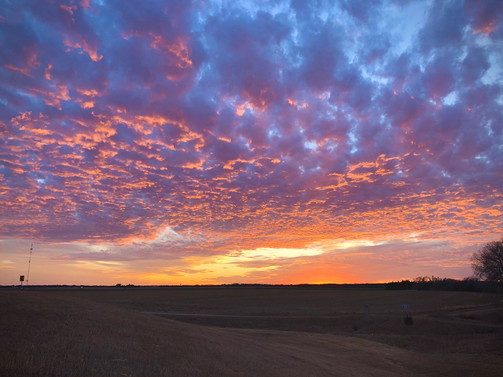 Sunset over open fields under a dramatic purple and orange cloud-filled sky