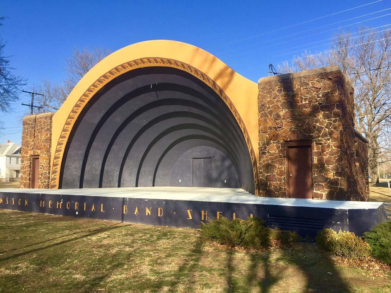 Outdoor amphitheater with a large arched stage and stone walls under a blue sky