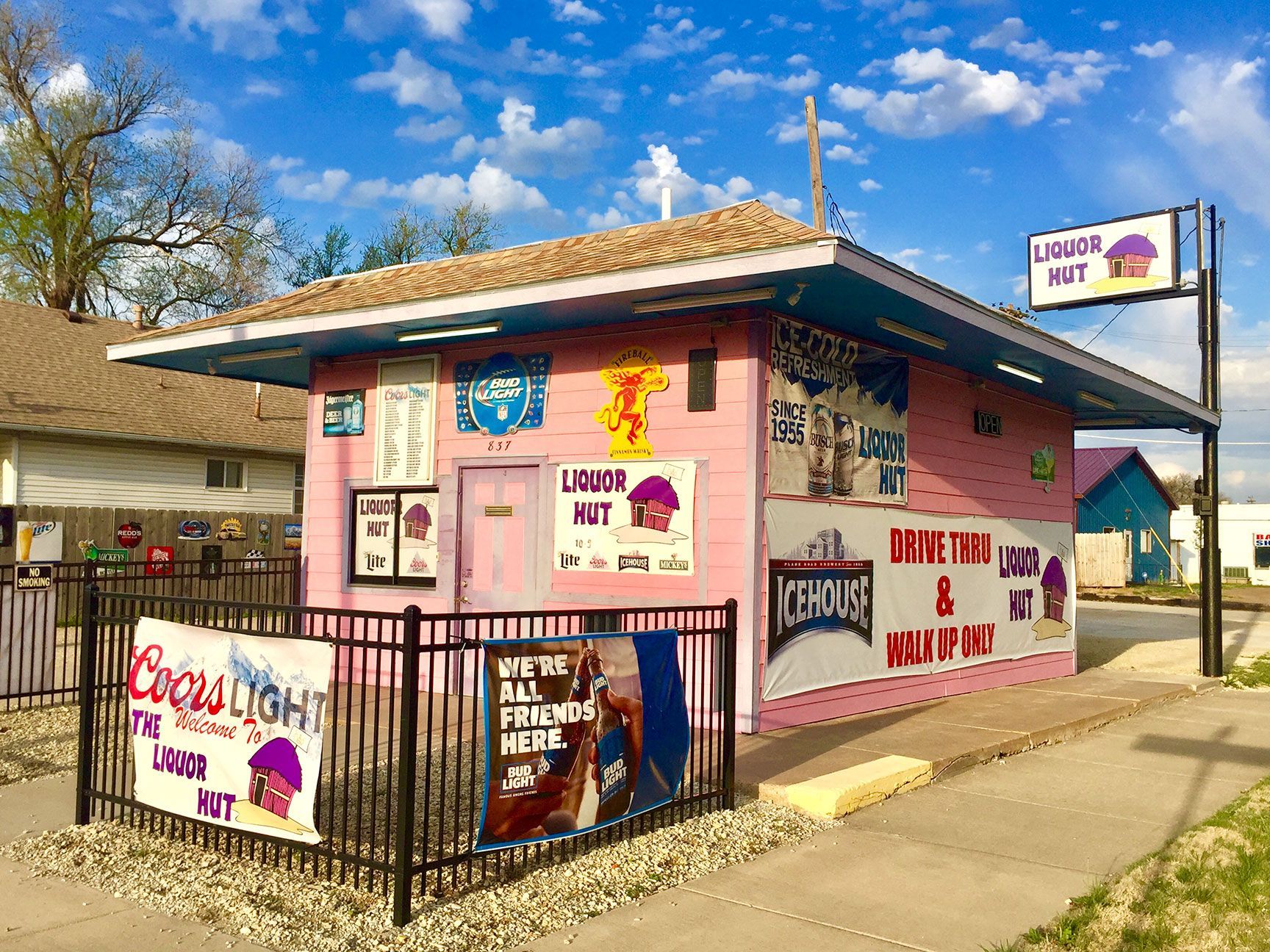 Pink roadside shop with Mexican food signs, black fence, and a blue sky with clouds